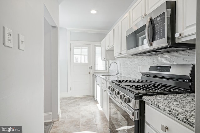 kitchen with tasteful backsplash, appliances with stainless steel finishes, light stone counters, white cabinetry, and a sink