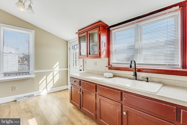 kitchen with light wood-style flooring, a sink, visible vents, vaulted ceiling, and light countertops