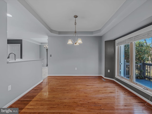 unfurnished dining area featuring baseboards, a tray ceiling, wood finished floors, and a notable chandelier