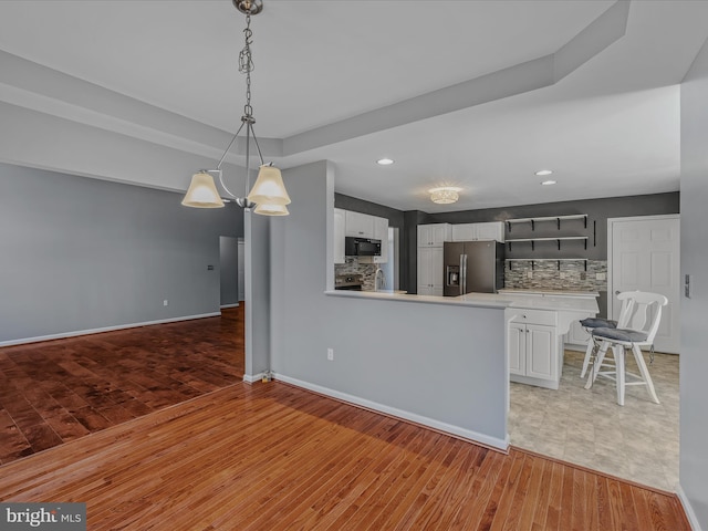 kitchen with black microwave, light countertops, stainless steel refrigerator with ice dispenser, and backsplash