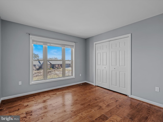 unfurnished bedroom featuring a closet, wood finished floors, visible vents, and baseboards