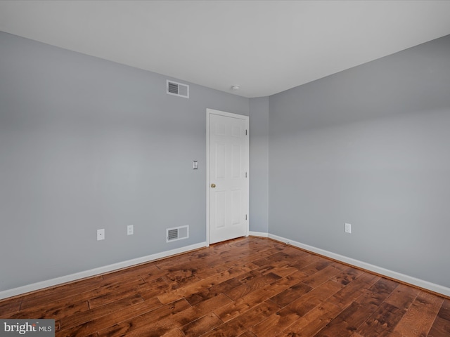 spare room featuring wood-type flooring, visible vents, and baseboards