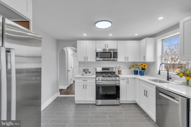 kitchen featuring stainless steel appliances, a sink, white cabinetry, light countertops, and backsplash