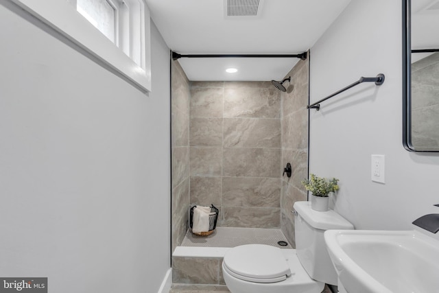 full bathroom featuring toilet, a sink, a tile shower, and visible vents