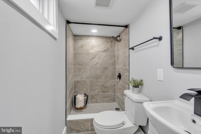 bathroom featuring a tile shower, toilet, a sink, and visible vents