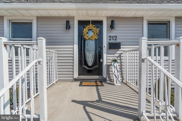 view of exterior entry featuring a shingled roof and covered porch