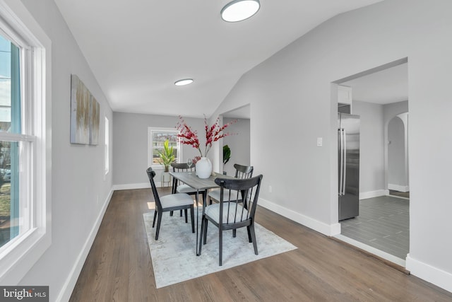 dining area with dark wood-type flooring, lofted ceiling, arched walkways, and baseboards