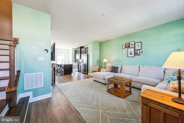 living room featuring visible vents, baseboards, dark wood finished floors, and stairway