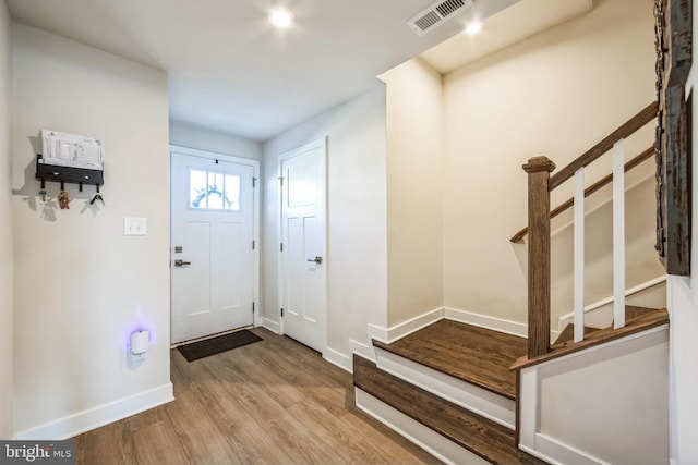 entryway with stairs, wood finished floors, visible vents, and baseboards