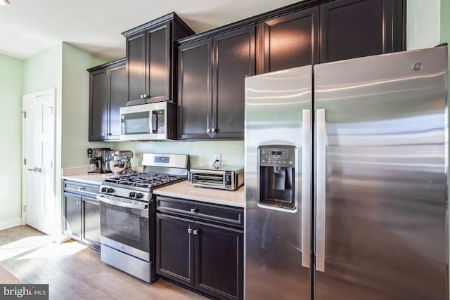 kitchen with light wood-type flooring, appliances with stainless steel finishes, a toaster, baseboards, and light countertops