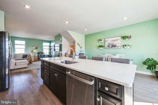 kitchen with a kitchen island with sink, a sink, open floor plan, dark wood-style floors, and stainless steel appliances