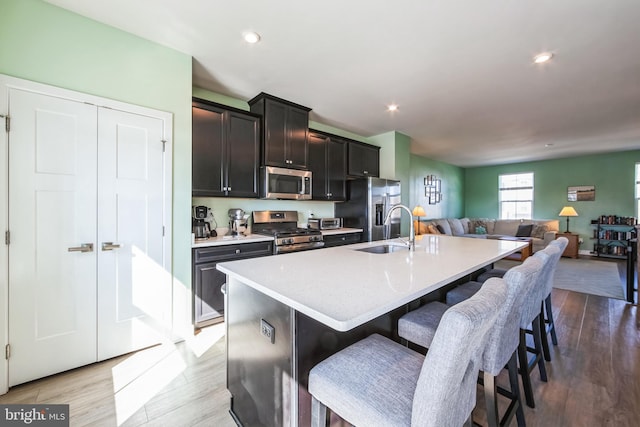 kitchen featuring a kitchen island with sink, a sink, appliances with stainless steel finishes, a kitchen breakfast bar, and open floor plan