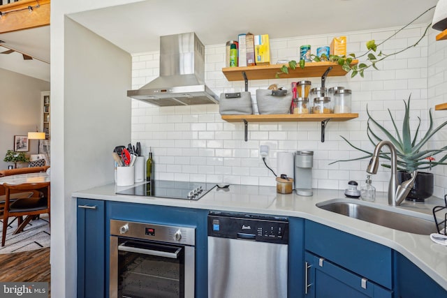 kitchen with a sink, light countertops, blue cabinetry, appliances with stainless steel finishes, and wall chimney exhaust hood