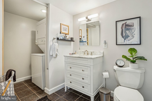 bathroom with stacked washer and dryer, toilet, vanity, tile patterned flooring, and baseboards