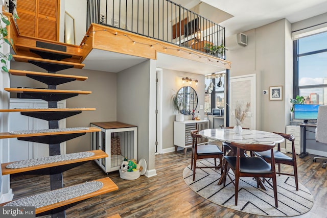 dining area featuring a high ceiling, a wall unit AC, wood finished floors, and baseboards