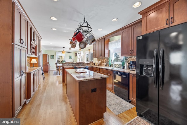 kitchen featuring black appliances, a sink, a peninsula, light wood finished floors, and decorative backsplash