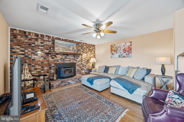 living room featuring visible vents, a wood stove, a ceiling fan, and wood finished floors