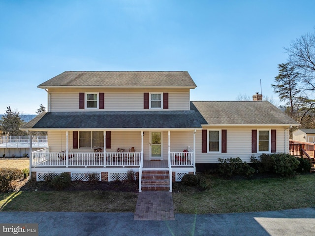 view of front of house with a front lawn, covered porch, roof with shingles, and a chimney