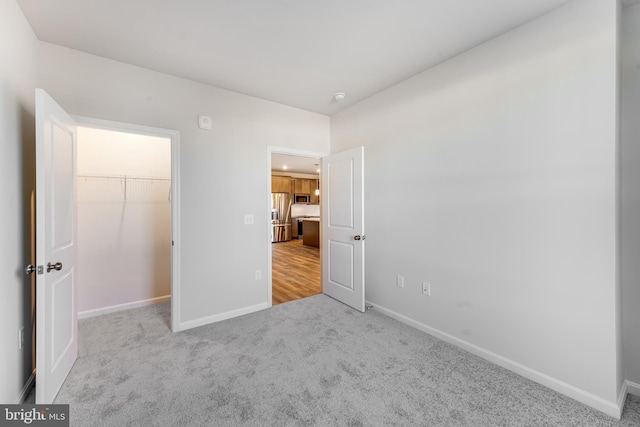 unfurnished bedroom featuring carpet, baseboards, a walk in closet, and stainless steel fridge with ice dispenser