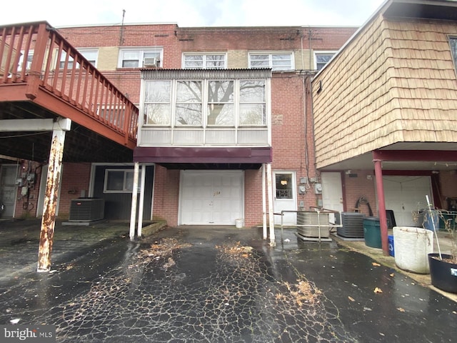 rear view of house featuring a garage, brick siding, aphalt driveway, and central air condition unit