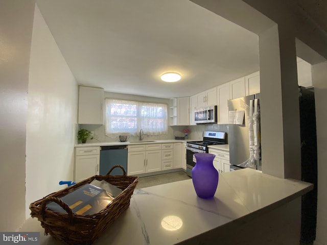 kitchen with appliances with stainless steel finishes, white cabinetry, a sink, and tasteful backsplash