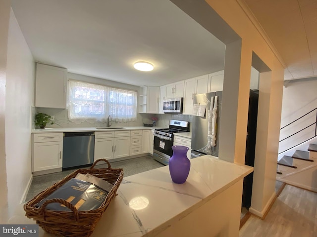 kitchen with white cabinets, decorative backsplash, stainless steel appliances, crown molding, and a sink