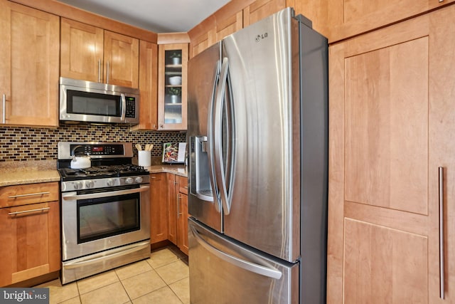 kitchen featuring decorative backsplash, glass insert cabinets, light stone countertops, stainless steel appliances, and light tile patterned flooring