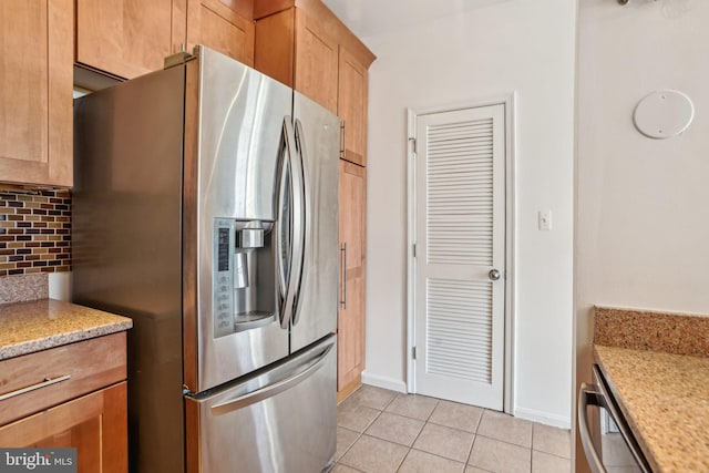 kitchen with light tile patterned floors, tasteful backsplash, appliances with stainless steel finishes, light stone countertops, and baseboards