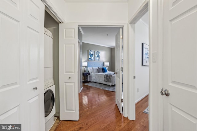 laundry room with laundry area, baseboards, ornamental molding, stacked washer / drying machine, and wood finished floors