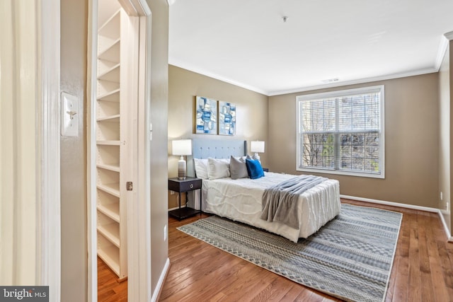 bedroom with ornamental molding, wood finished floors, and baseboards