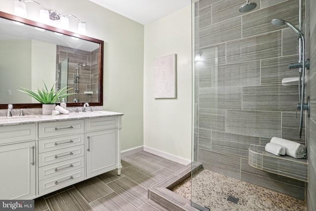 bathroom with baseboards, double vanity, a sink, and a shower stall