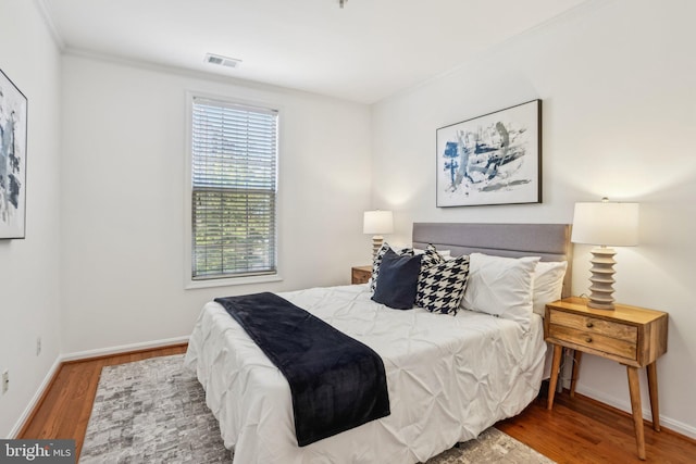 bedroom with visible vents, crown molding, baseboards, and wood finished floors