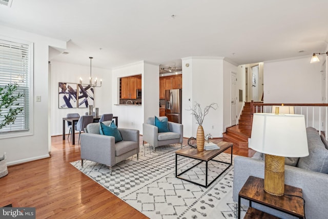 living area with light wood finished floors, an inviting chandelier, ornamental molding, baseboards, and stairs