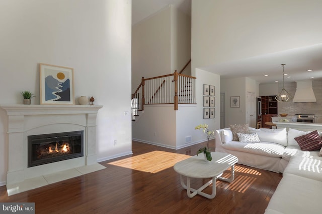 living room featuring baseboards, visible vents, a fireplace with flush hearth, wood finished floors, and stairs