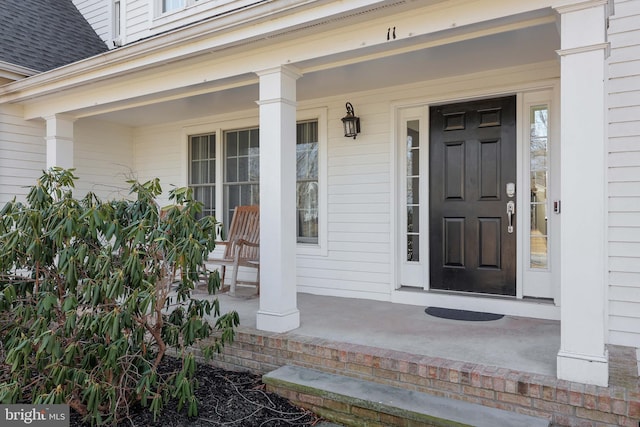 entrance to property with a porch and roof with shingles