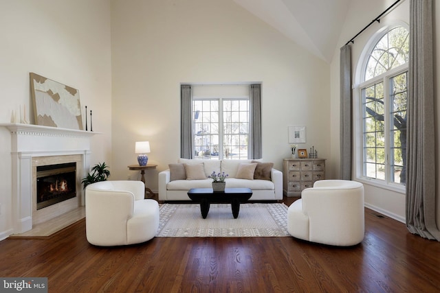 living area with baseboards, a lit fireplace, high vaulted ceiling, and wood finished floors