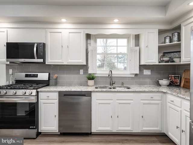 kitchen featuring a sink, backsplash, white cabinetry, appliances with stainless steel finishes, and light wood finished floors