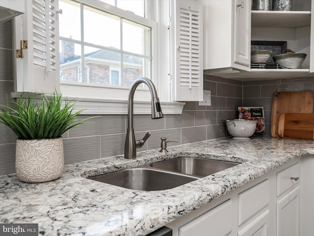 kitchen featuring white cabinetry, decorative backsplash, light stone countertops, and a sink