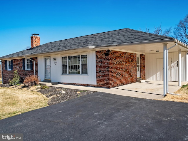 single story home featuring a carport, driveway, a chimney, and brick siding