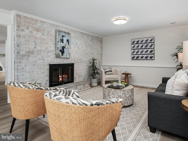 living area with wood finished floors, a fireplace, baseboards, and ornamental molding