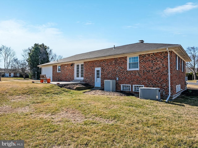 rear view of house featuring brick siding, central AC unit, a lawn, french doors, and a patio area