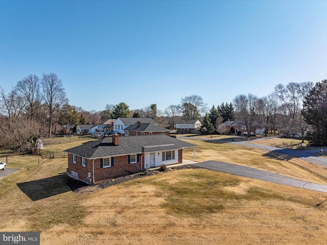 view of front facade with a front yard, fence, driveway, brick siding, and a residential view