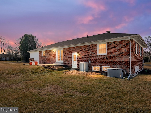 back of property featuring brick siding, central AC unit, and a lawn