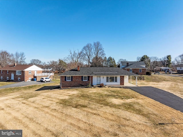 view of front of home featuring brick siding, a residential view, a front yard, a chimney, and driveway