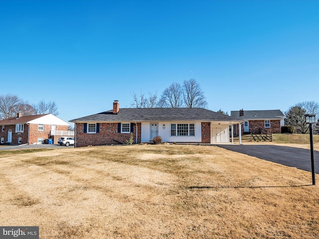 ranch-style home with an attached carport, a front yard, driveway, a chimney, and brick siding