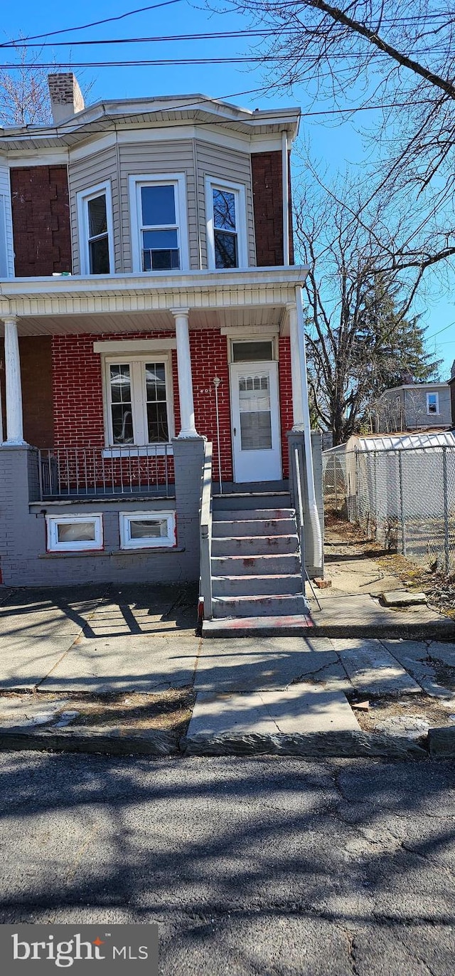 view of front facade with a chimney, fence, a porch, and brick siding