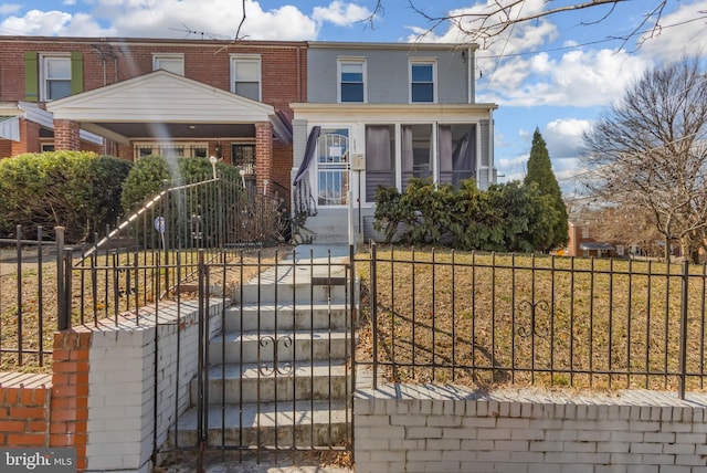 view of front of property with a fenced front yard, a sunroom, brick siding, and a gate