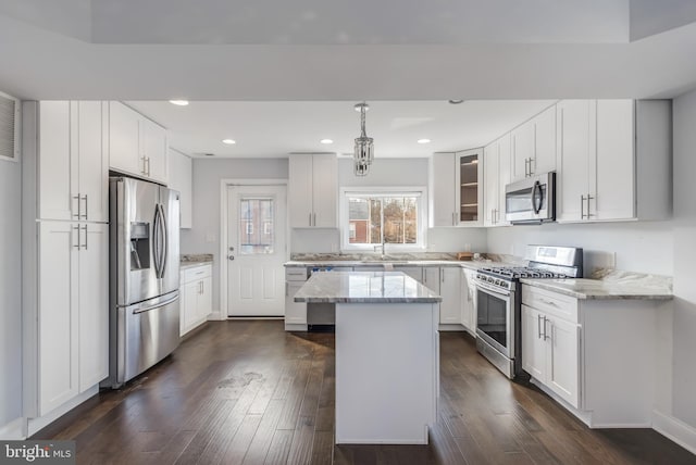 kitchen with appliances with stainless steel finishes, light stone counters, dark wood-style flooring, and a center island