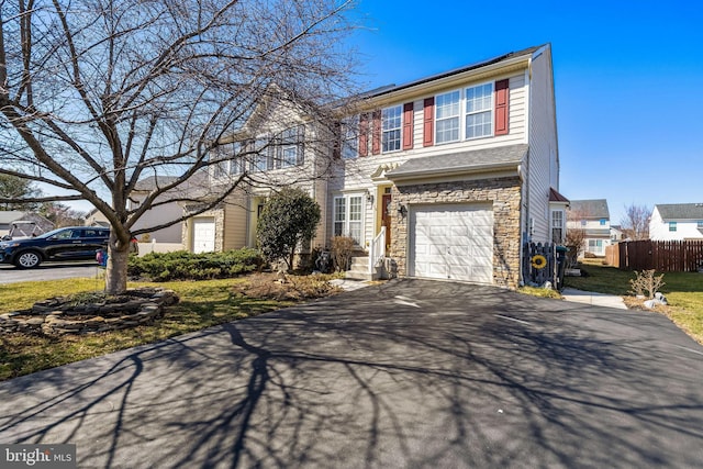 view of front of home with driveway, stone siding, roof mounted solar panels, fence, and an attached garage