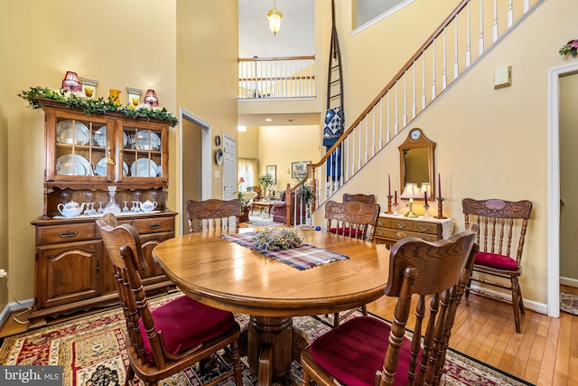 dining room featuring a towering ceiling, baseboards, wood finished floors, and stairs